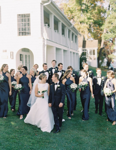 Bride and Groom walking and laughing with their bridal party, all in black, walking behind them outside