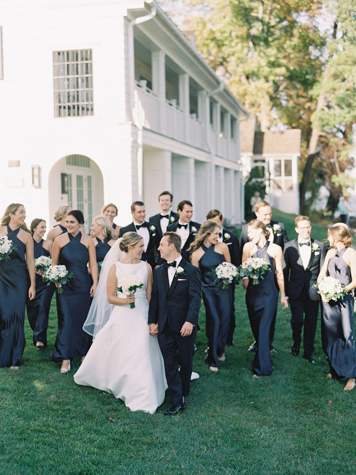 Bride and Groom walking and laughing with their bridal party, all in black, walking behind them outside